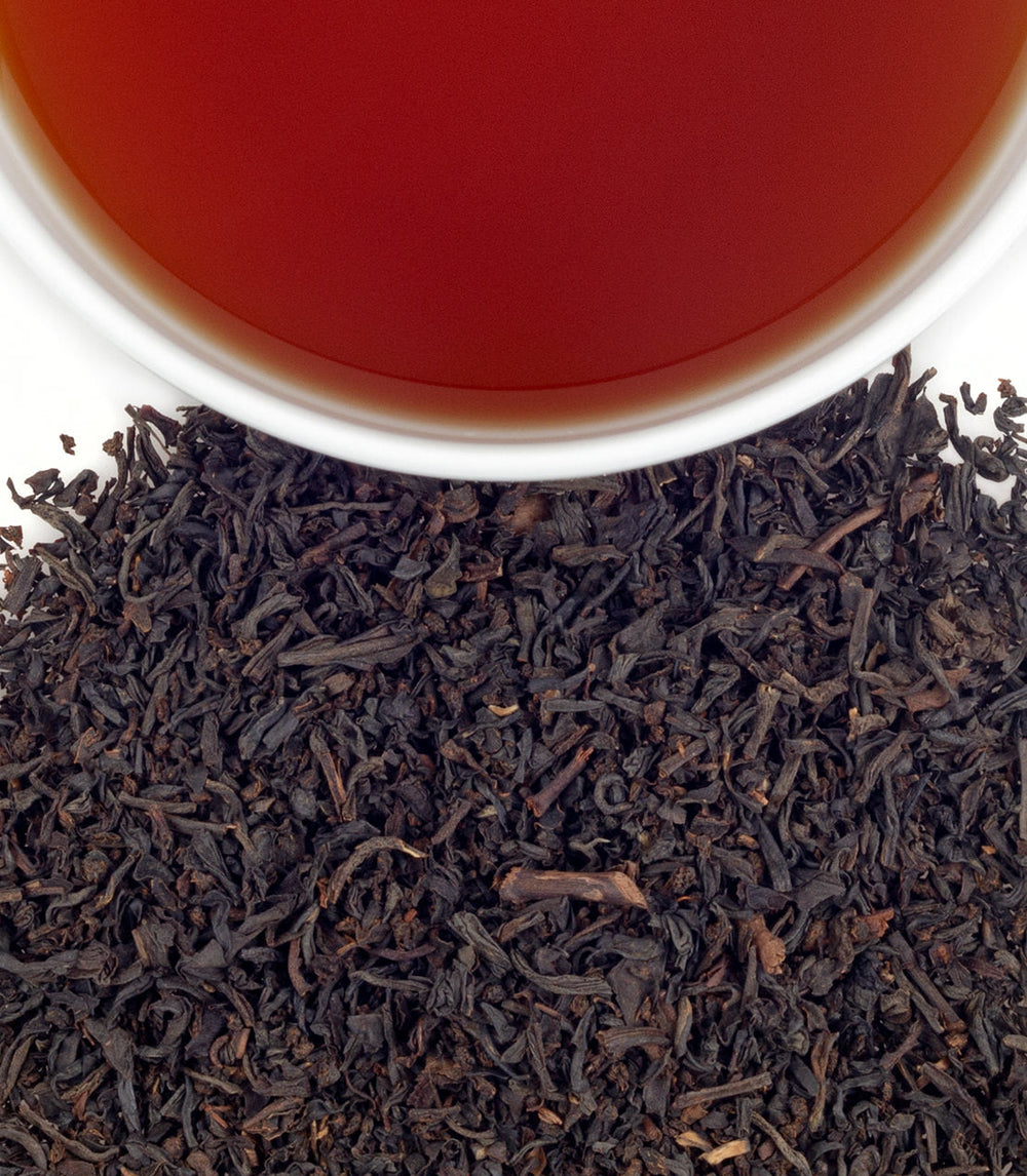 Dry black tea leaves with a cup of red tea in the background.
