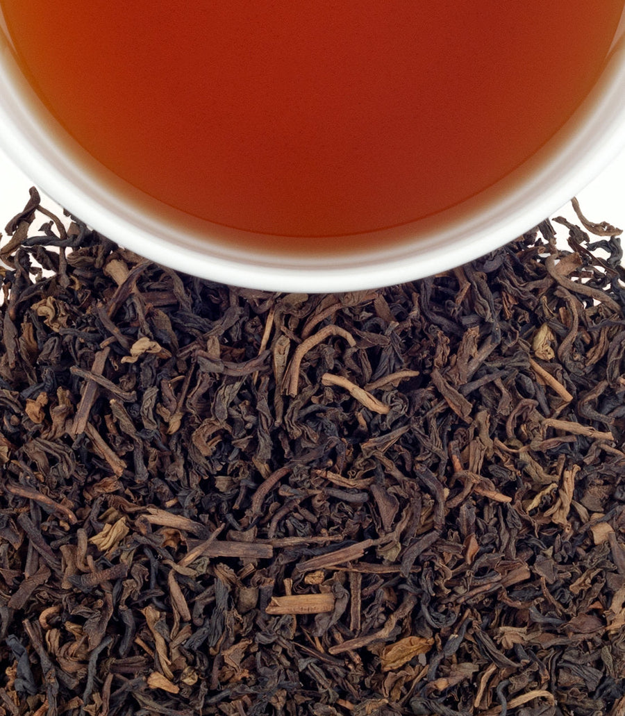 Close-up of tea leaves with a cup of tea in the background