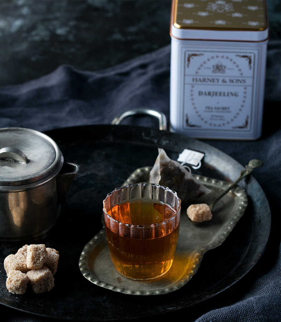 Teacup with Harney and Sons Darjeeling tea tin on a dark surface.