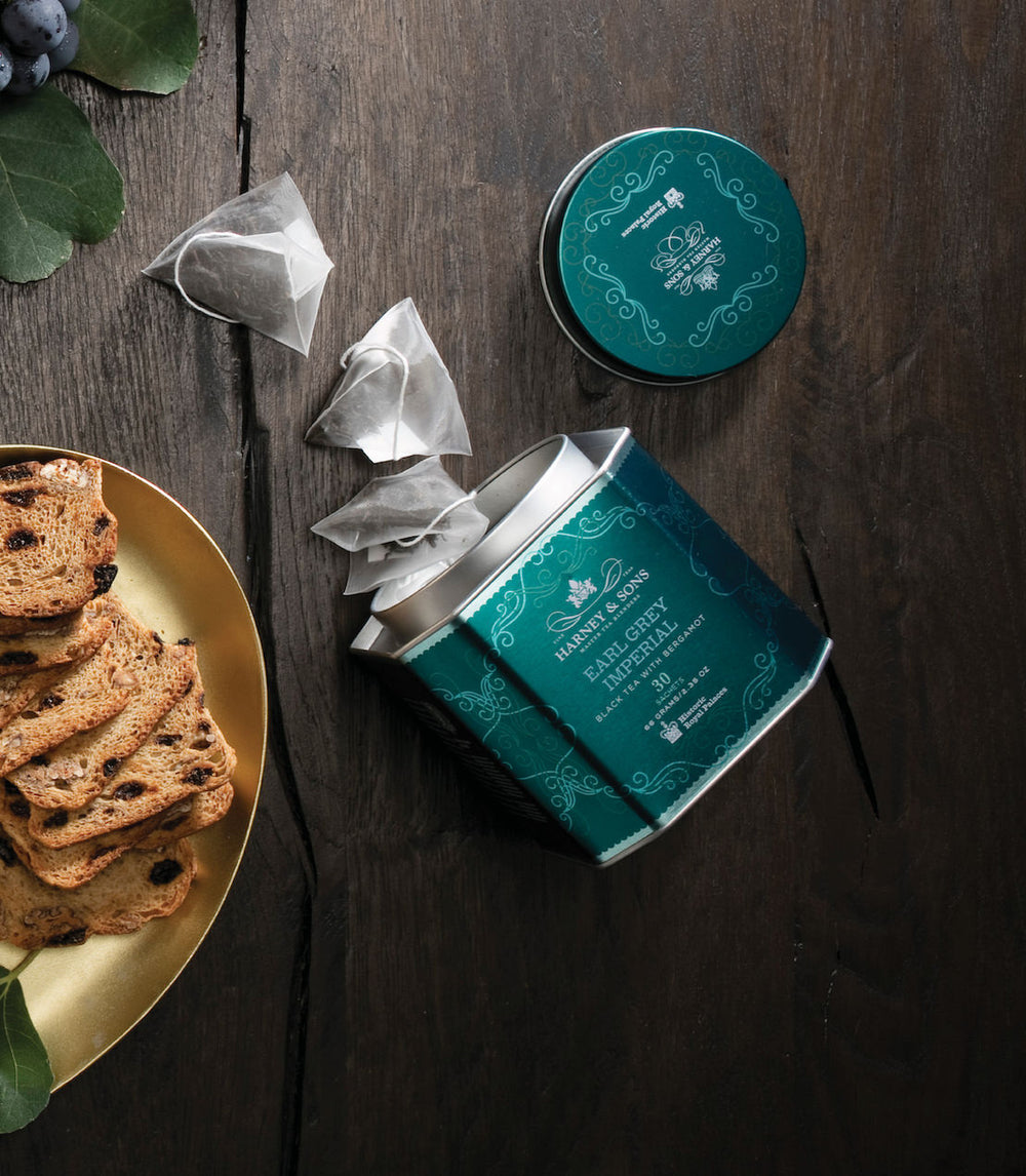 Open teal tea canister with tea bags and cookies on a wooden surface.