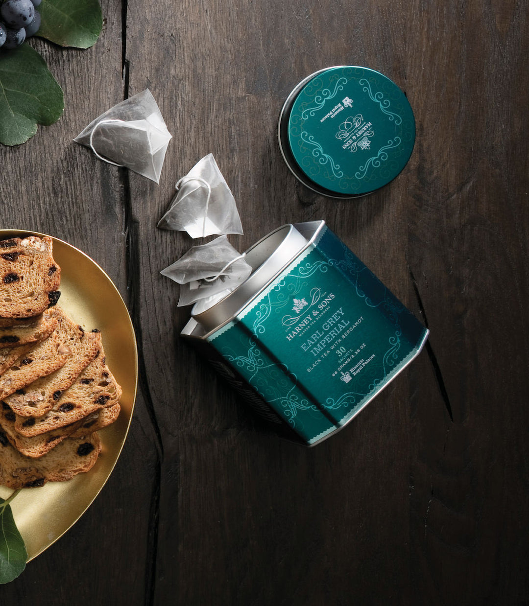 Open teal tea canister with tea bags and cookies on a wooden surface.