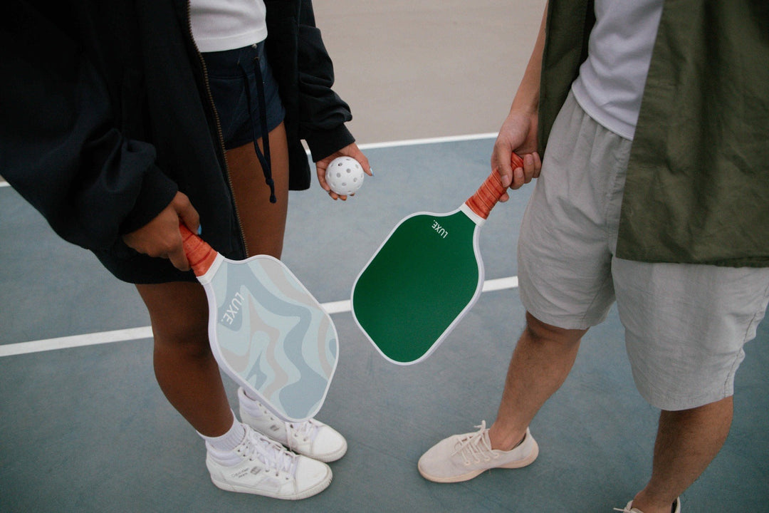 Two people holding pickleball paddles on a court