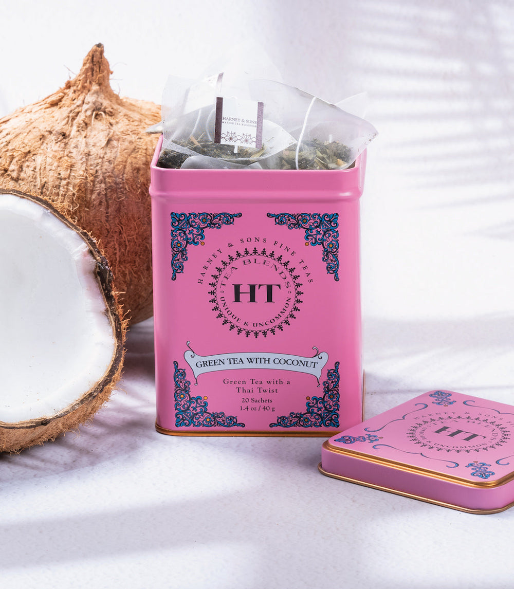 Pink tea canister labeled Green Tea with Coconut next to a coconut on a white background.