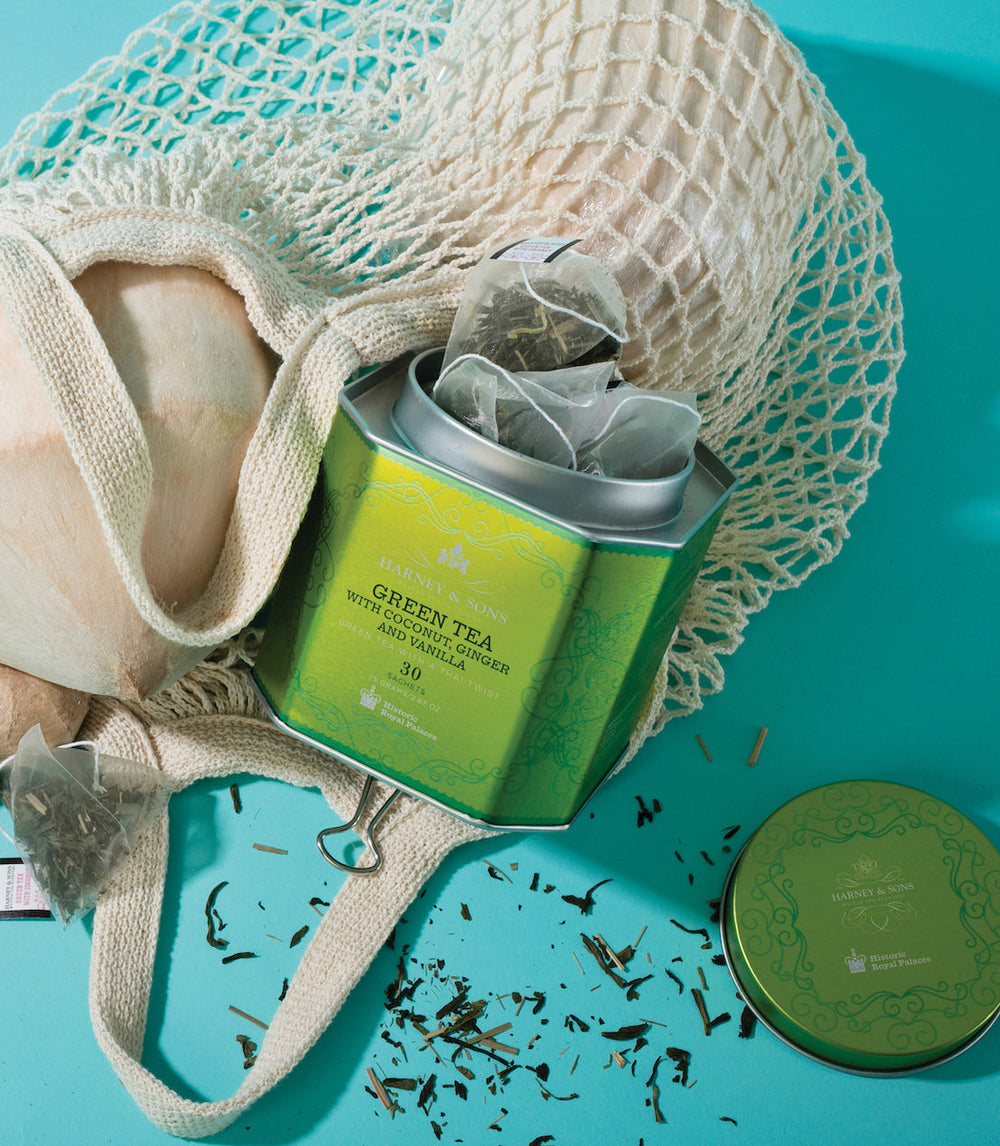 Green tea canister with tea bags on a turquoise surface, surrounded by a mesh bag.