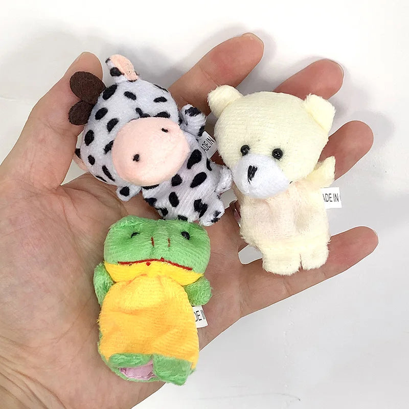 Three small plush toys (cow, bear, frog) held in a hand on a white background.