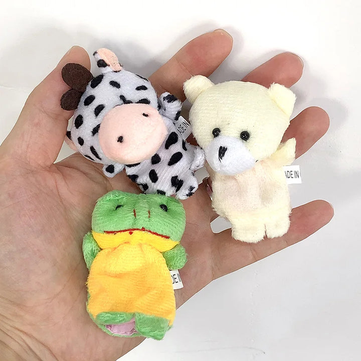 Three small plush toys (cow, bear, frog) held in a hand on a white background.