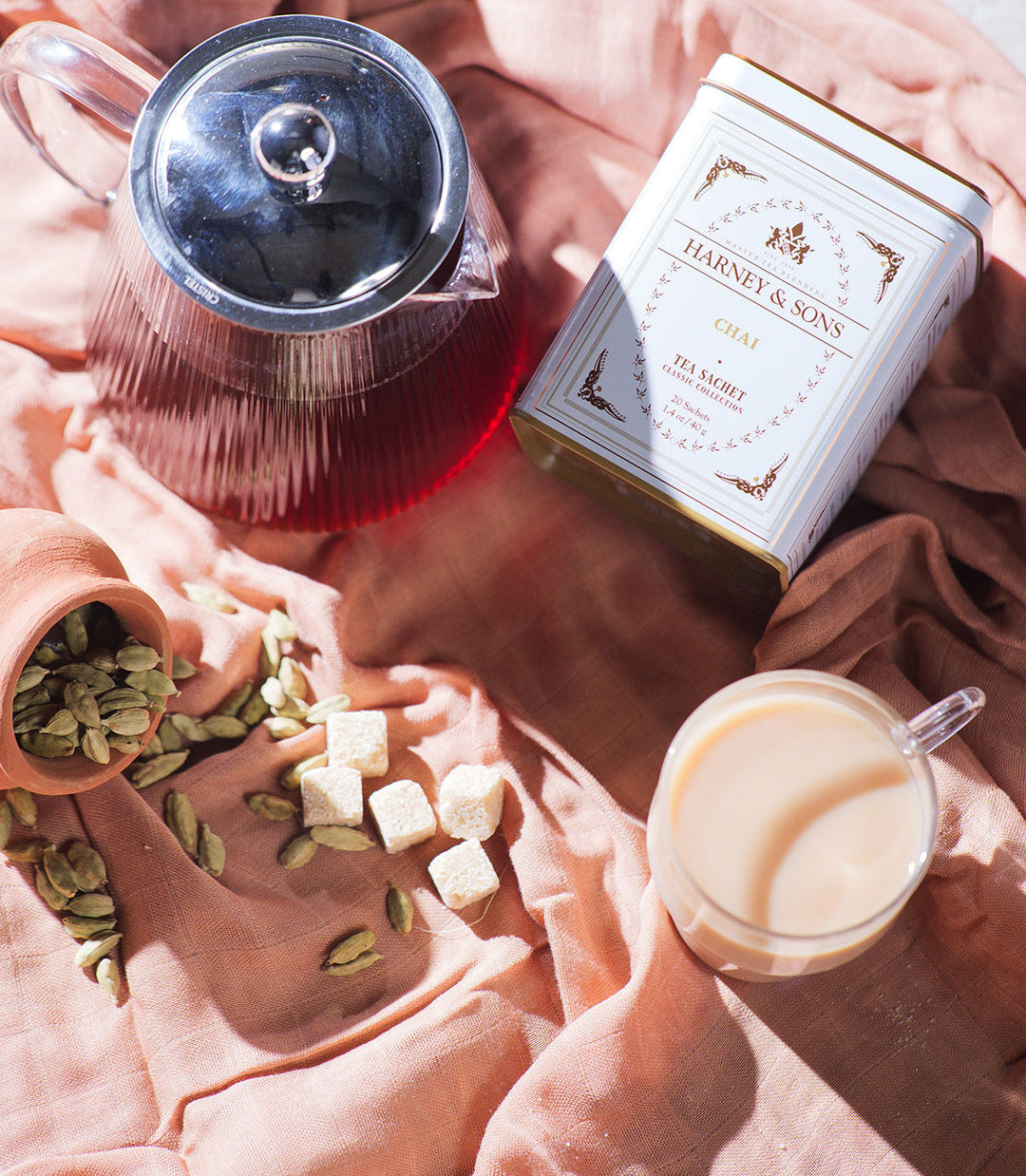 Tea-making setup with Harney and Sons tea box, teapot, and cup on a pink fabric background.