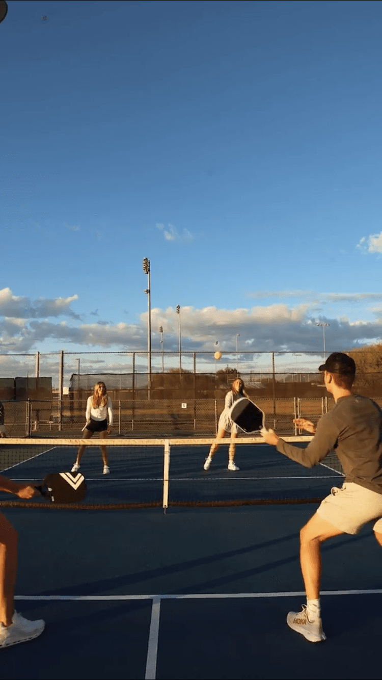 Three people playing tennis on a court with a clear blue sky.