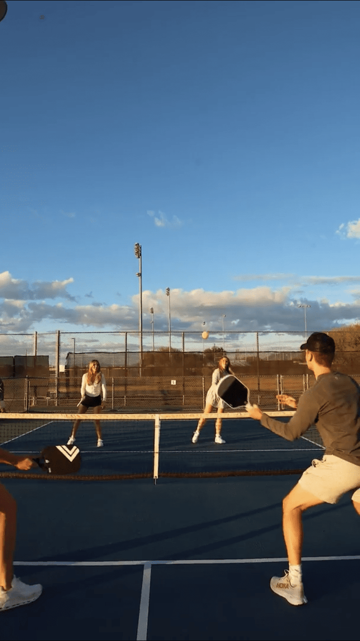 Three people playing tennis on a court with a clear blue sky.