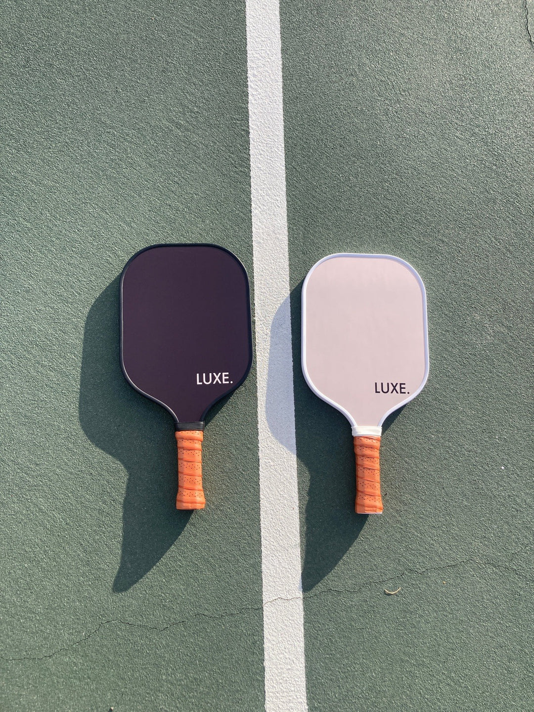 Two pickleball paddles with orange handles on a green court.