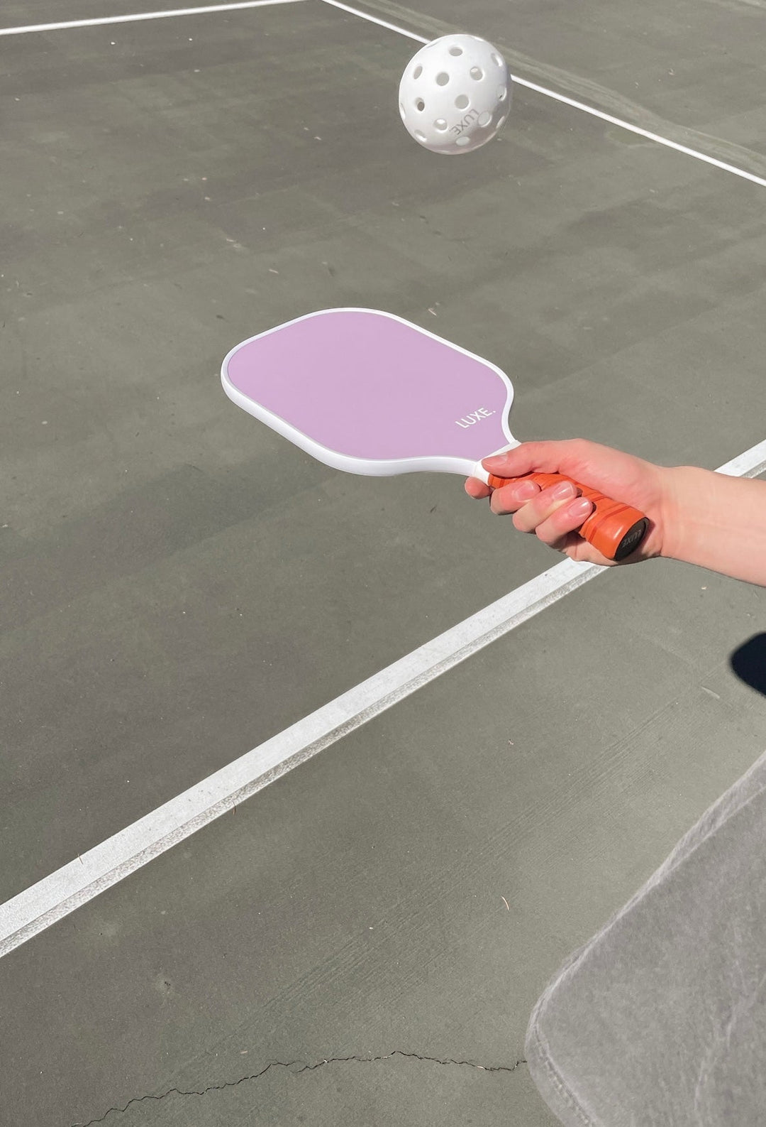 Person holding a purple pickleball paddle on a pickleball court with a white ball in motion.