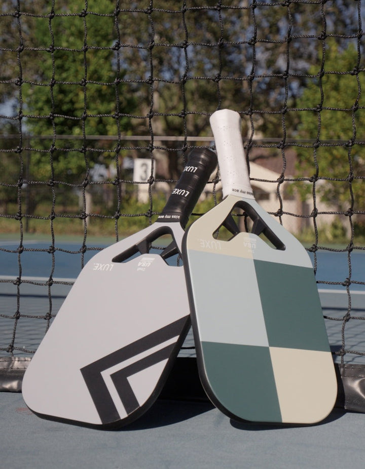 Two pickleball paddles on a court with a net in the background.