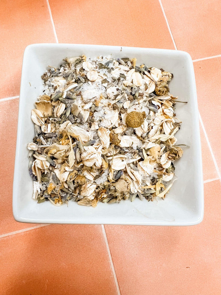 White square bowl filled with dried herbs on a terracotta tiled floor.