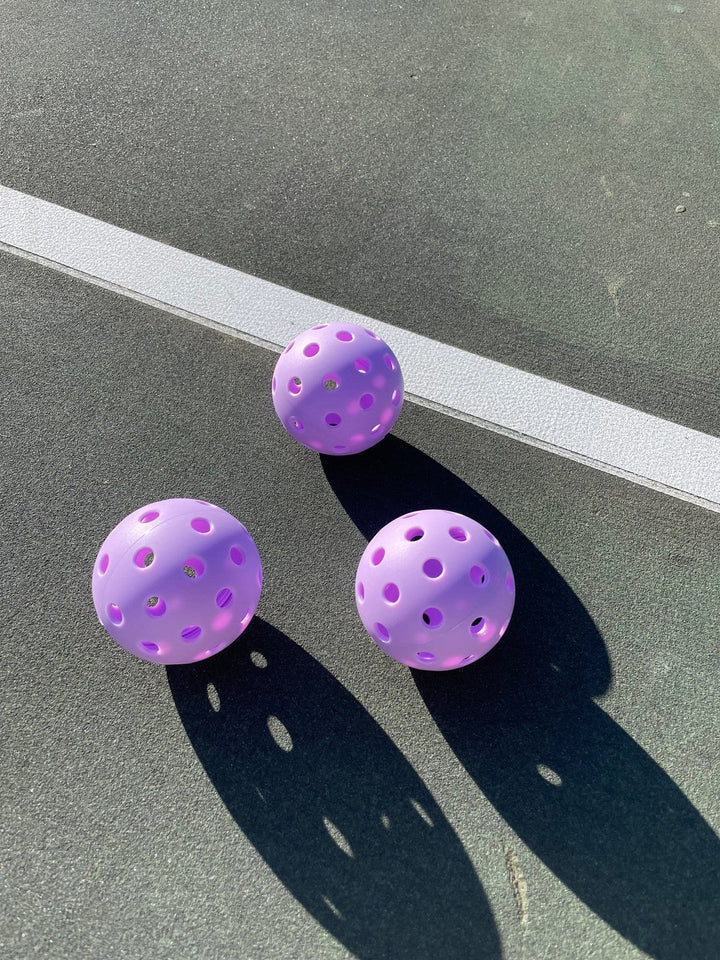 Three purple perforated balls on a gray surface
