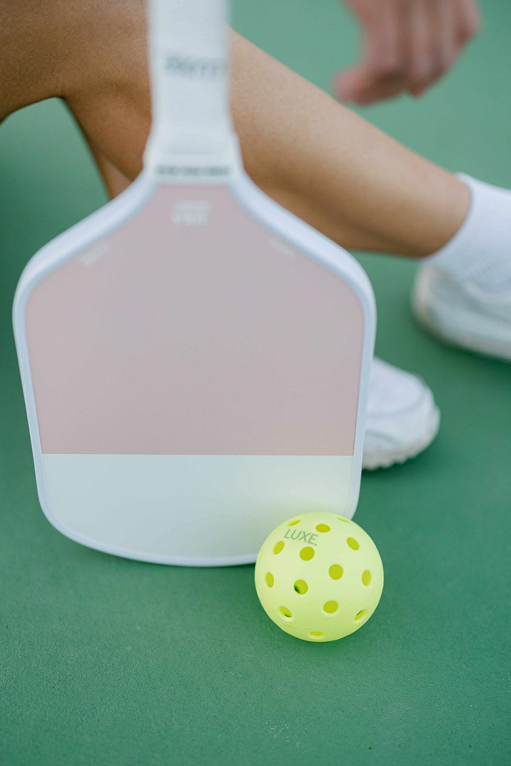 Pink and white paddle with a yellow ball on a green surface.