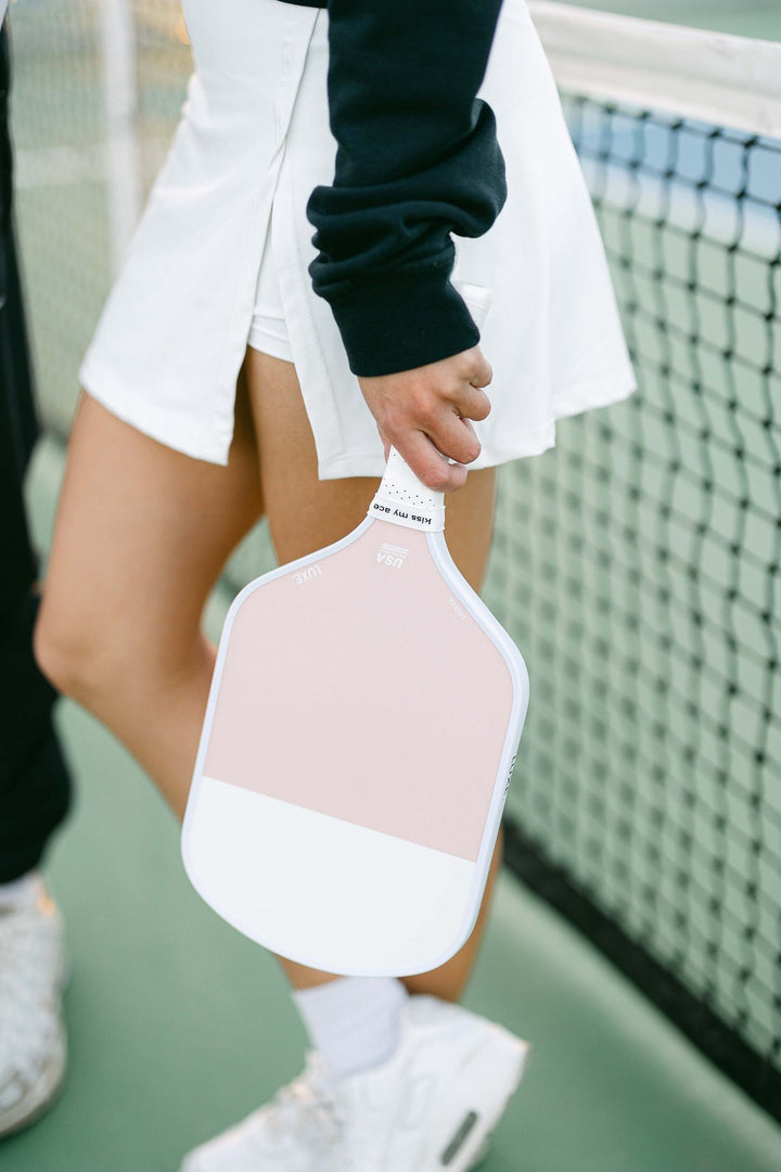 Person holding a pink and white paddle on a tennis court.