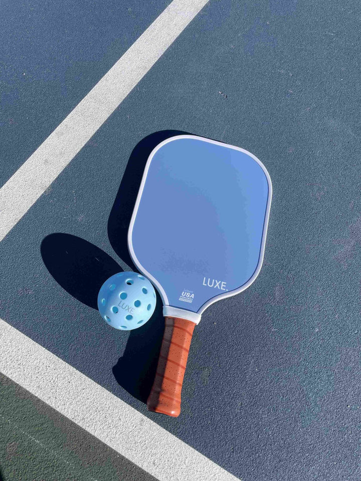 Blue pickleball paddle with brown handle on a court.