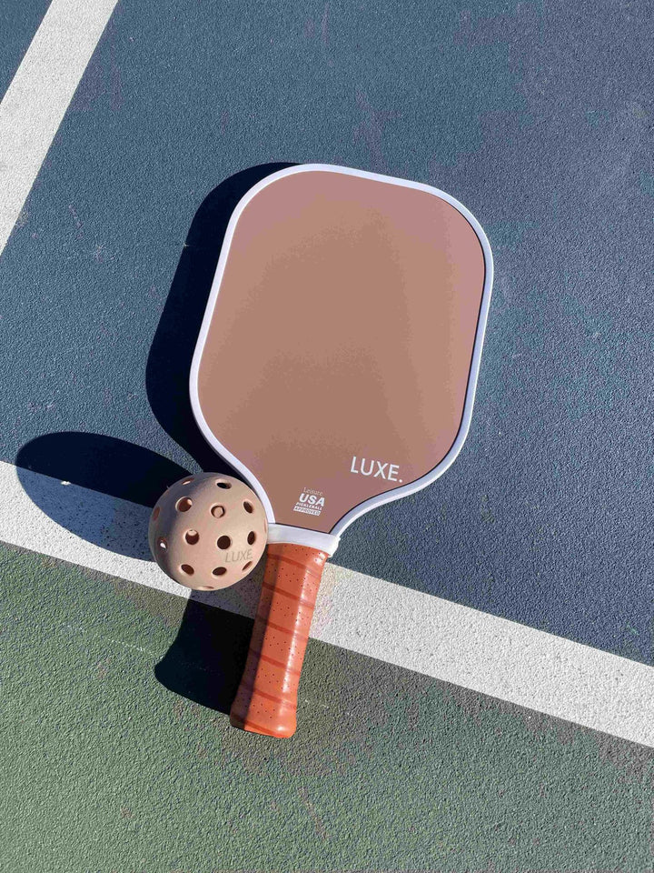 Pickleball paddle with brown face and red handle on a green court.