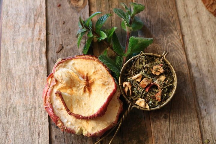 Dried apple slices and a small bowl of tea leaves on a wooden surface.