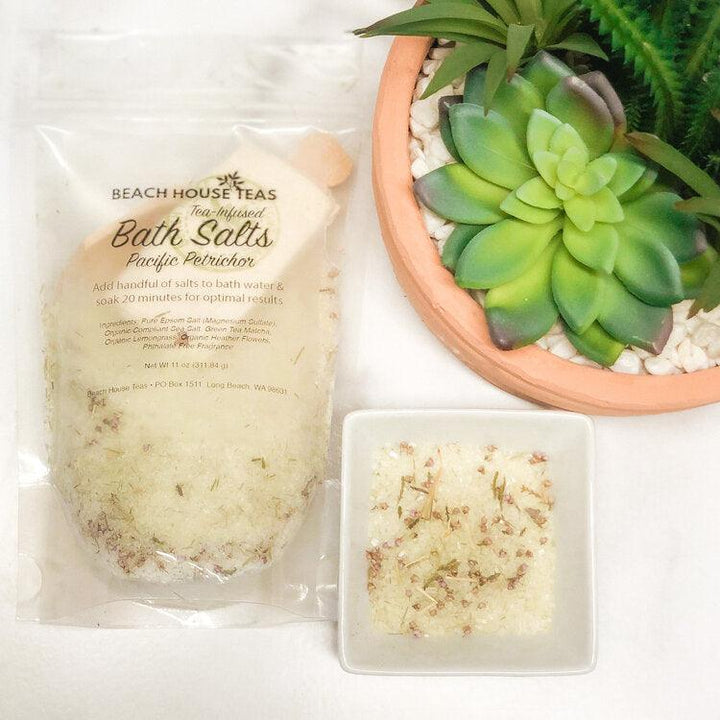 Beach House Teas Pacific Petrichor bath salts with a small dish of bath salts and a potted plant on a white surface.