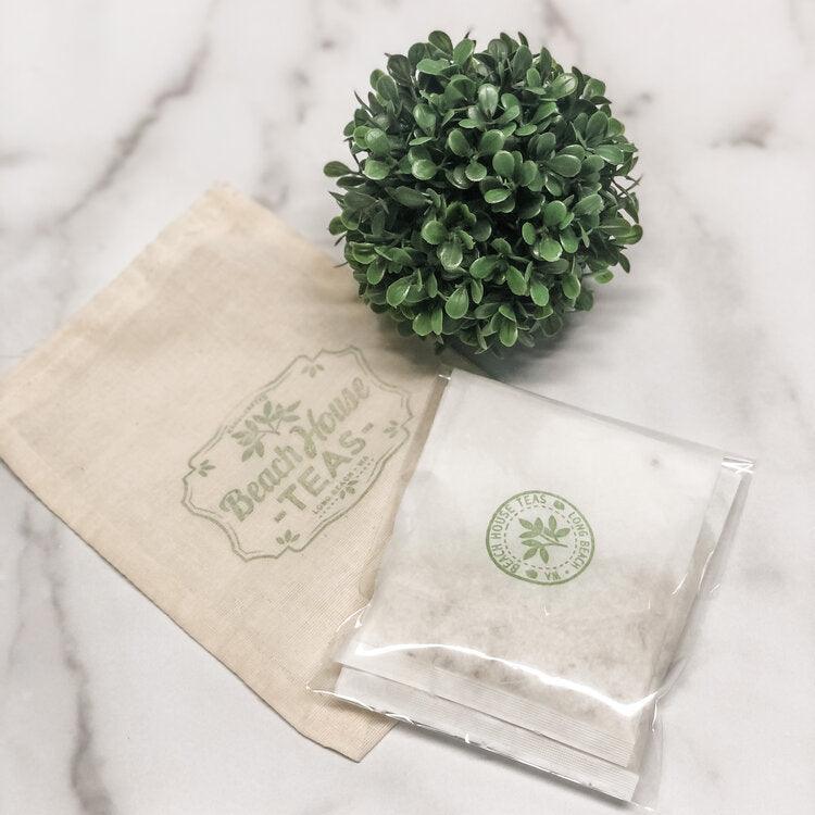 Tea bags with a brand logo on a marble surface with a small green plant.