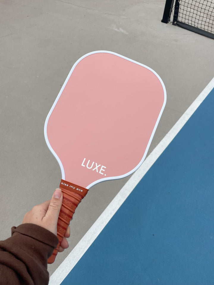 Pink pickleball paddle with LUXE branding held on a court.
