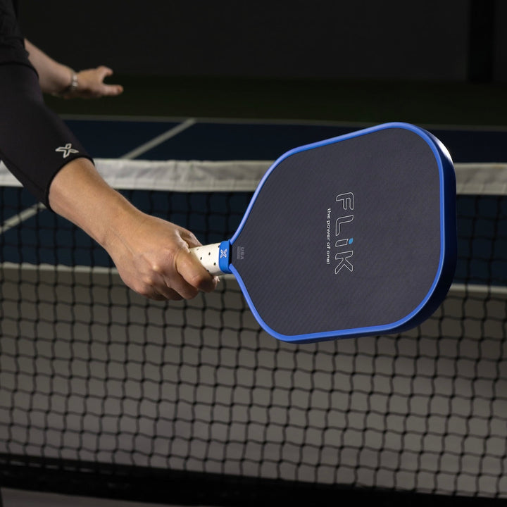 Person holding a blue and black pickleball paddle with FLIK branding on a court.