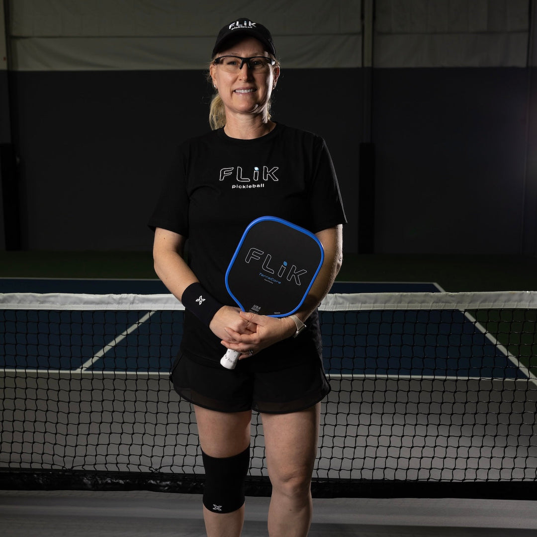 Person holding a pickleball paddle with Flik branding on a pickleball court.