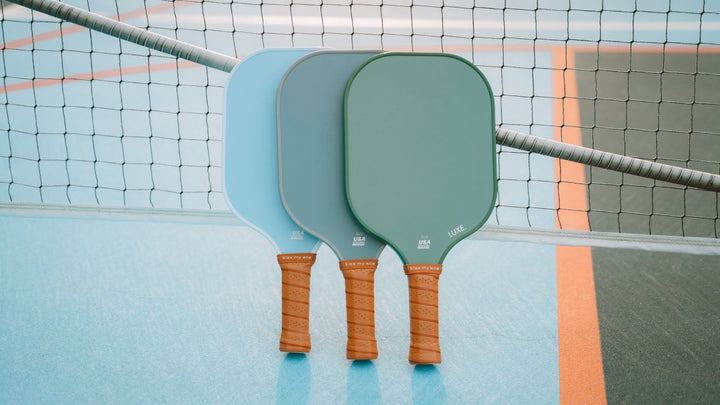 Two pickleball paddles on a court with a net in the background.