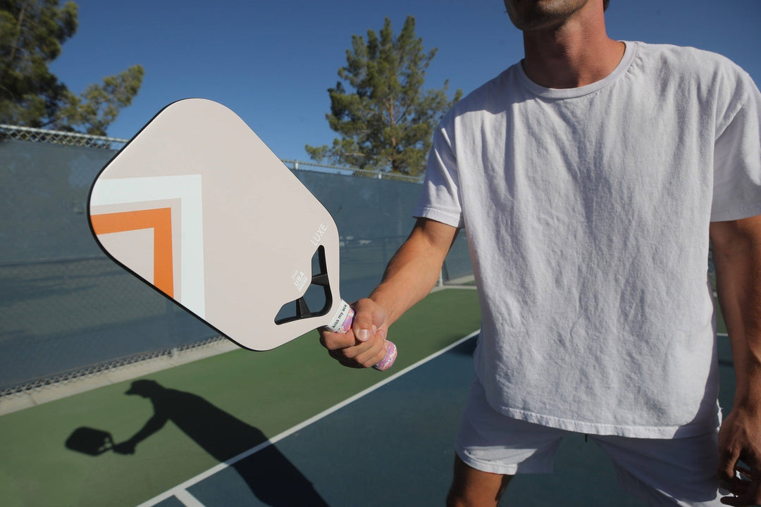 Person holding a pickleball paddle on a court with trees in the background.