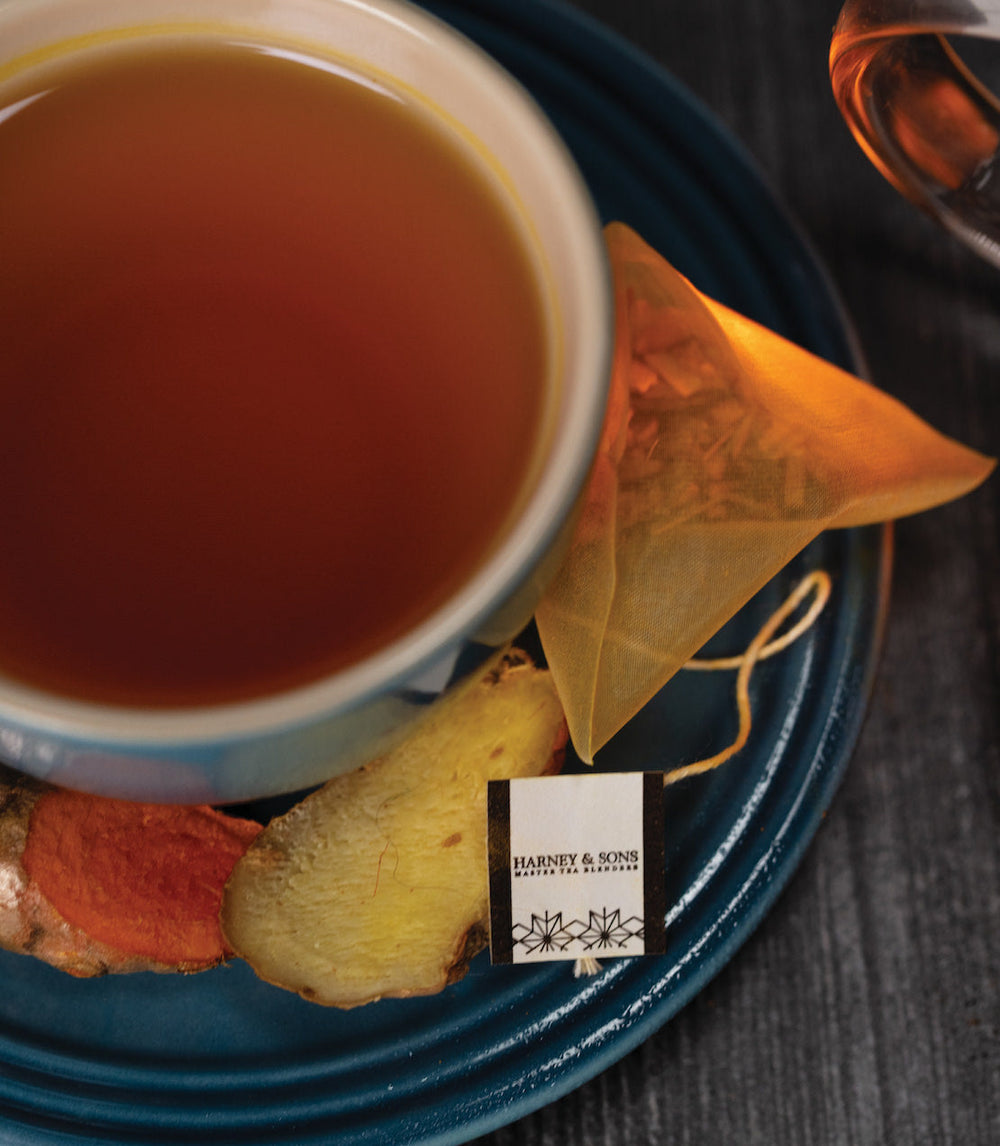 Tea cup with tea bag, ginger root, and a label on a blue plate.