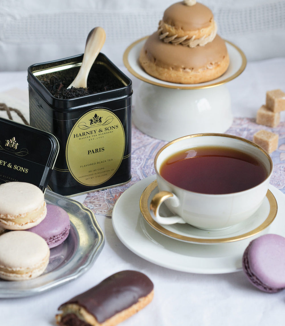 Teacup with Harney and Sons tea, macarons, and pastries on a white surface.