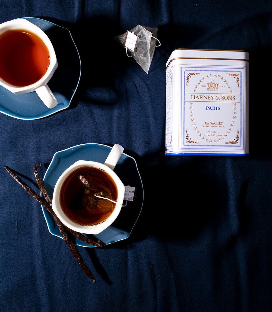 Two cups of tea with a Harney and Sons tea canister on a dark blue fabric background.