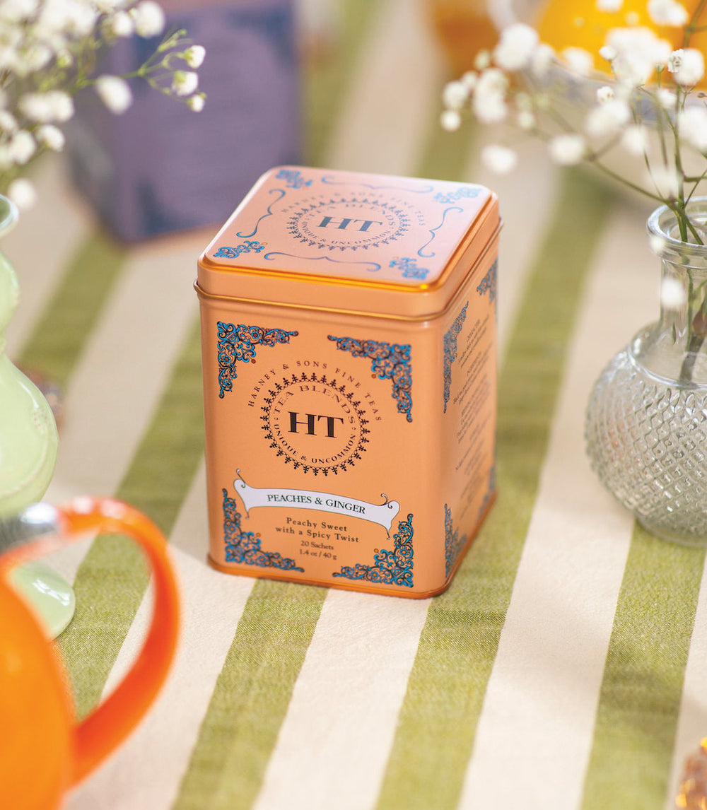 Orange tea tin with HT branding on a table with flowers and a mug.
