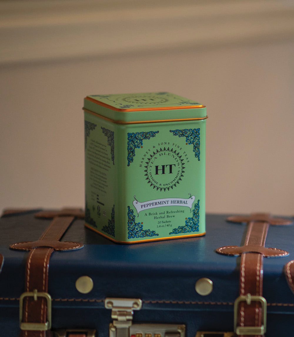 Green tea tin labeled HT on a vintage suitcase with a plain background