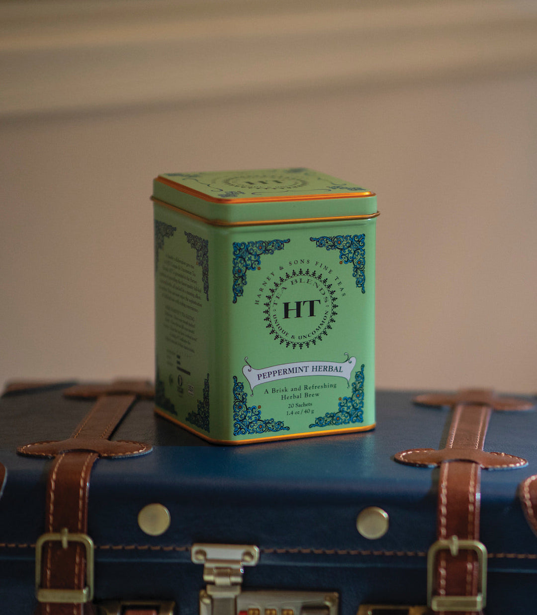 Green tea tin labeled HT on a vintage suitcase with a plain background