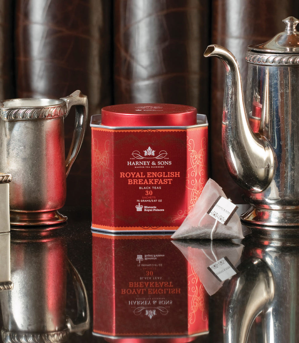 Red tea canister labeled Harney and Sons Royal English Breakfast with silver teacup and teapot in the background.