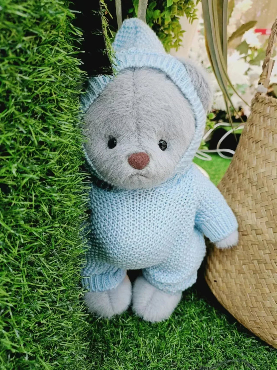 Stuffed teddy bear in a blue knitted outfit on grass.