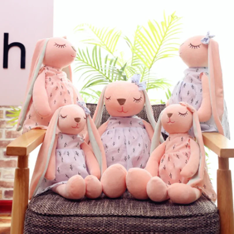 Set of pink plush bunnies with dresses on a chair with plants in the background.