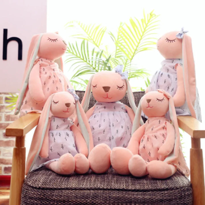 Set of pink plush bunnies with dresses on a chair with plants in the background.