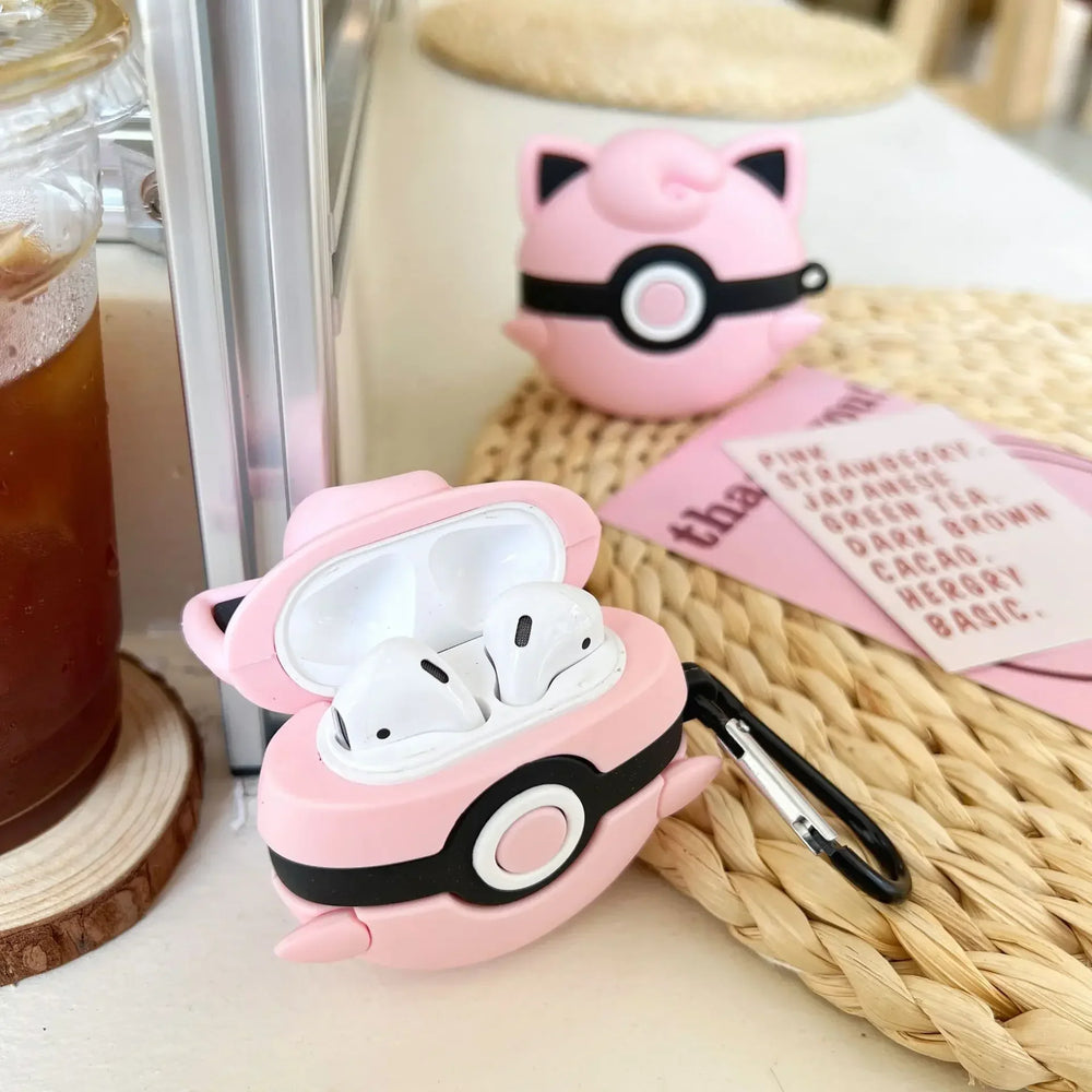 Pink air pod case with a carabiner on a table with a drink and small plush toy in the background.