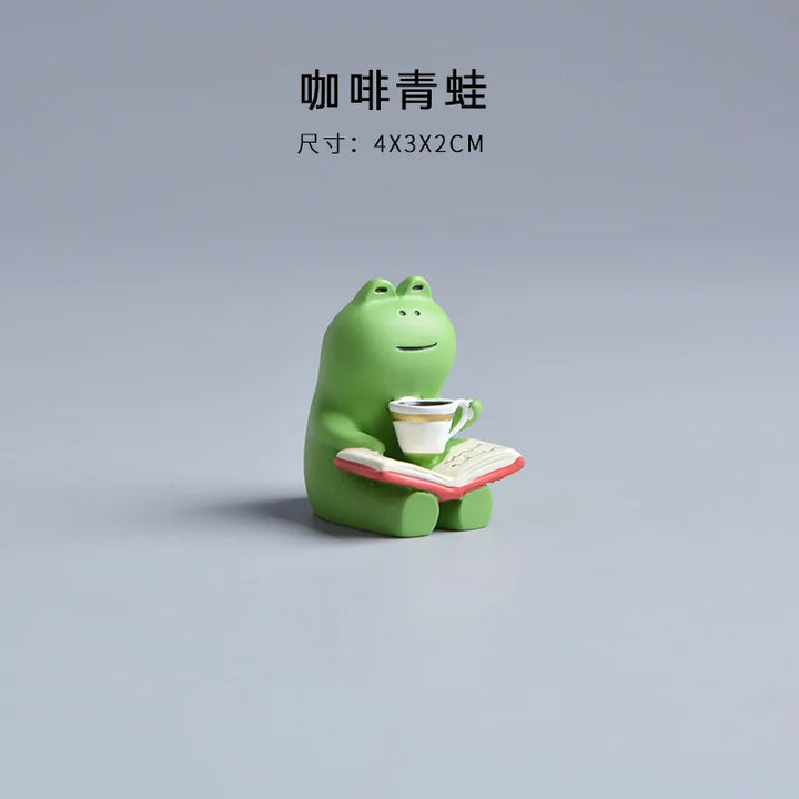 Green frog figurine holding a cup and book on a gray background.