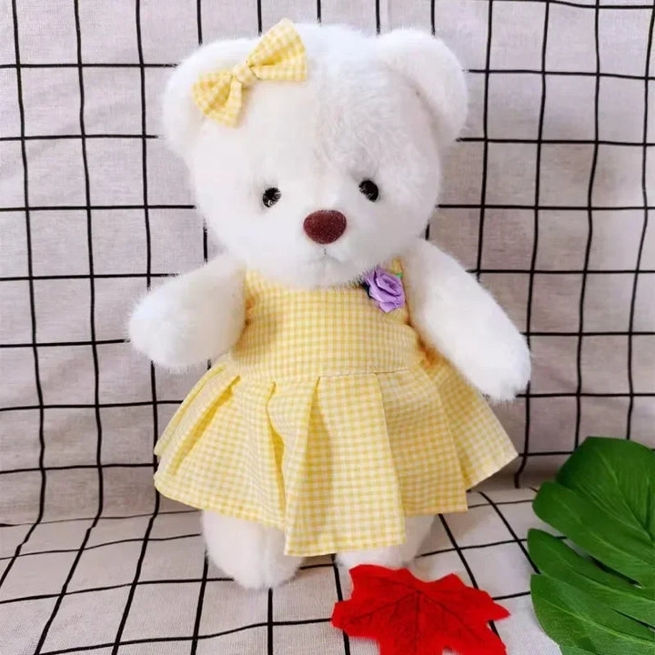 White teddy bear in a yellow dress with a purple flower on a checkered background.