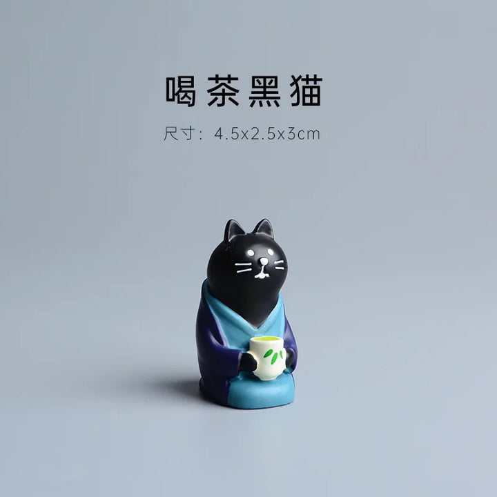 Black cat figurine holding a teacup on a gray background.