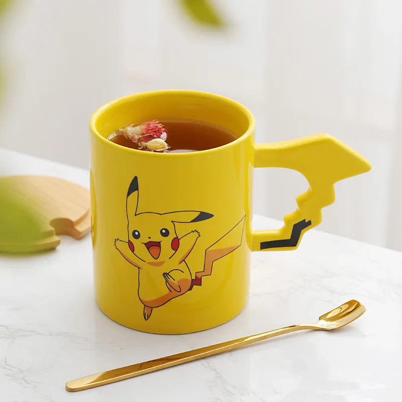 Yellow mug with Pikachu design, filled with tea, on a white surface with a gold spoon.