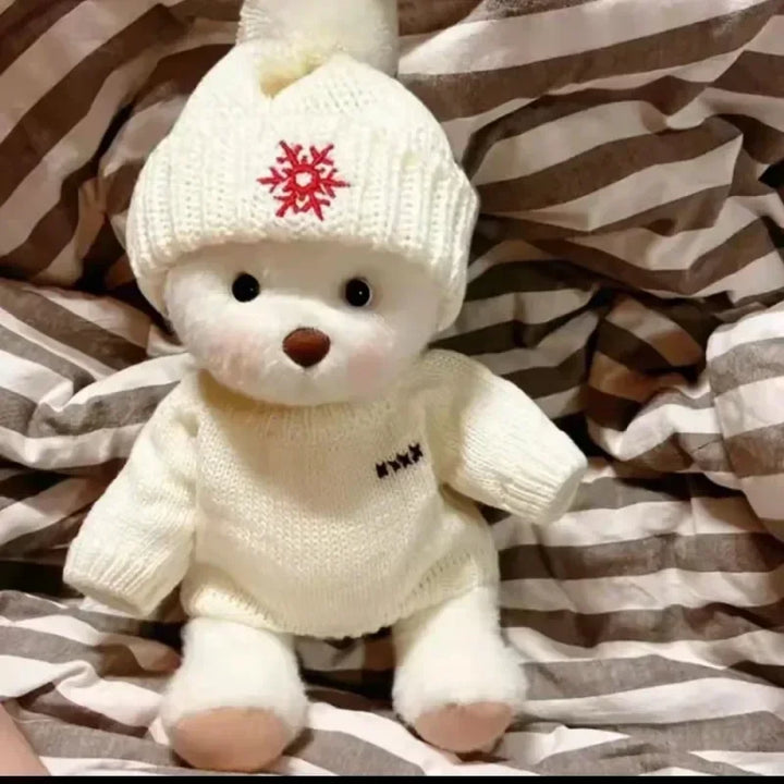 White teddy bear wearing a knitted hat with a red snowflake design on a striped fabric background.
