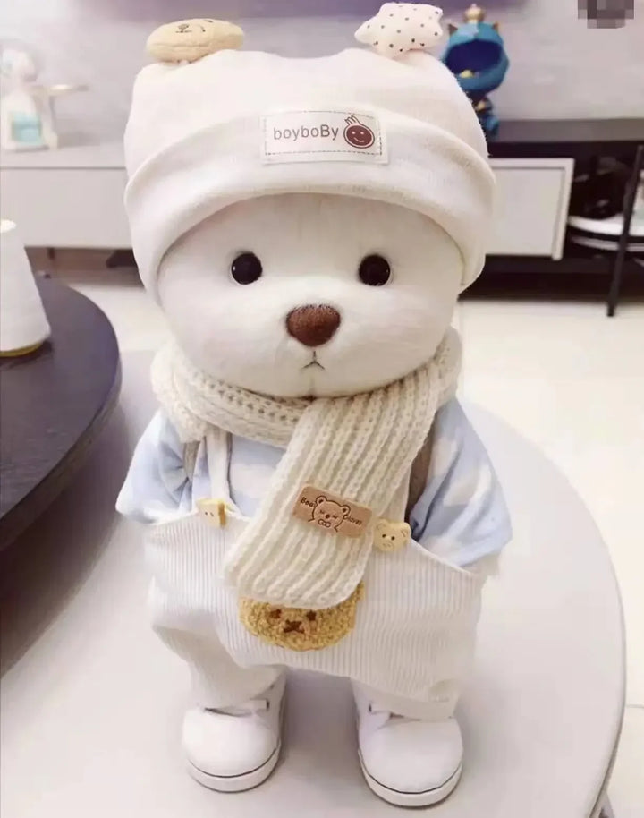 Teddy bear wearing a white hat, scarf, and overalls with a visible brand logo.
