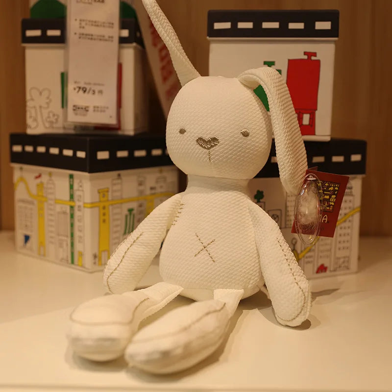 White plush toy rabbit with a neutral expression on a surface with blurred boxes in the background.