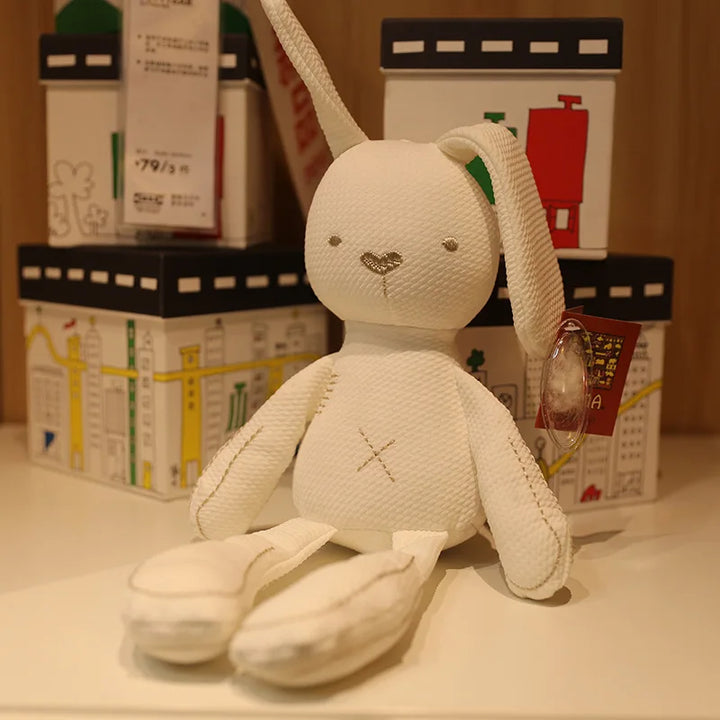 White plush toy rabbit with a neutral expression on a surface with blurred boxes in the background.