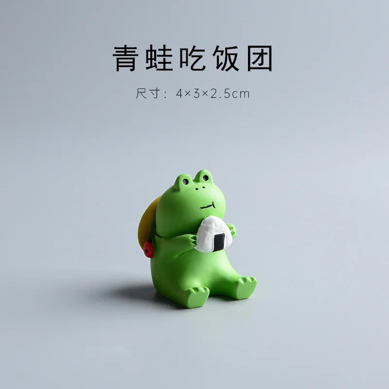Green frog figurine holding a white ball on a light gray background.